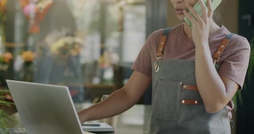 Woman in Apron Works on Laptop While on Phone