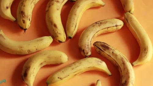 Ripe delicious wet bananas rotate clockwise on a black plate on a yellow background