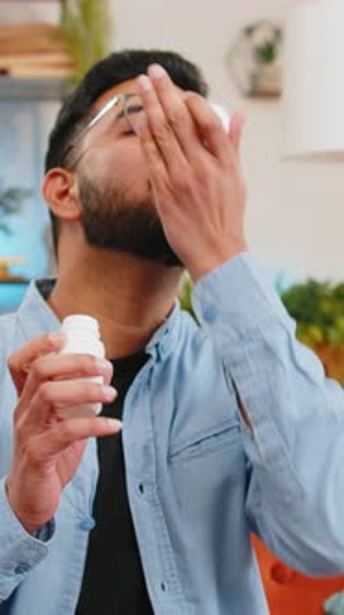 Indian Ill Sick Man Taking Medicine Antibiotic Pill with Water at Home Sofa Health Care Pharmacy