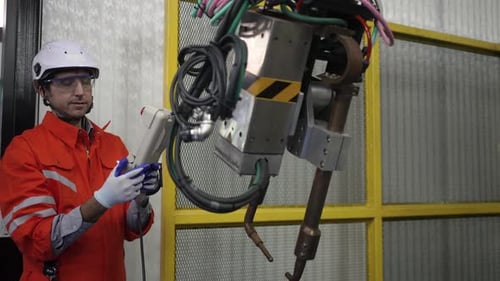 Blue collar workers at workshop with welding robot arm for automotive industry.