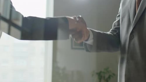 Handshake of Business People behind Glass Office Wall
