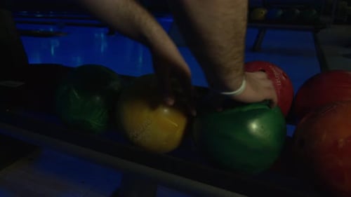 Eine Hand, die eine grüne Bowlingkugel vom Ball aufhebt, kehrt beim Nachtbowling zurück