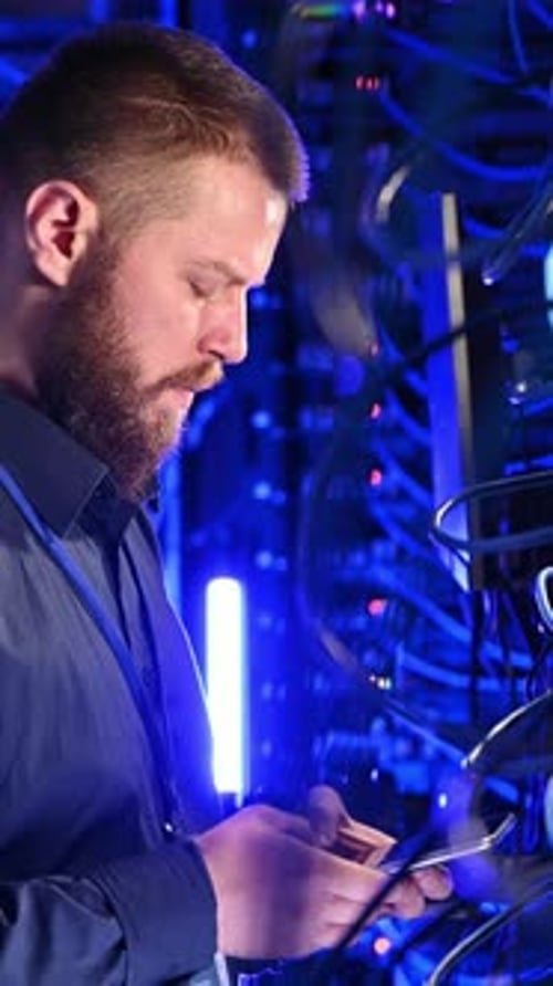 Male Using Phone in Server Room with Blue Lights
