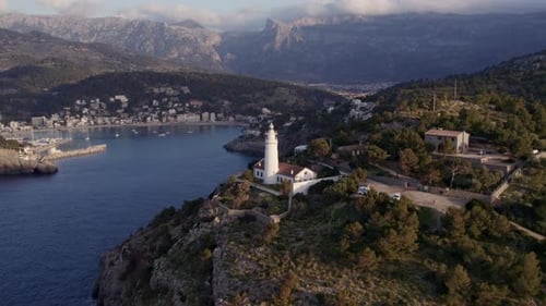 Aerial view of sunset over lighthouse, sea, cliff, and town in Mallorca, Spain.