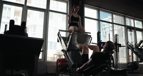 Man Using Leg Press With Spotter in Gym
