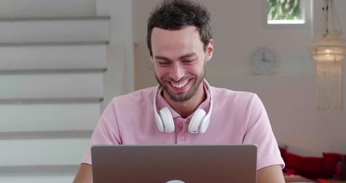 Front View of a Cheerful Young Man Wearing Pink Pastel Tshirt and Wireless Headphones on Neck