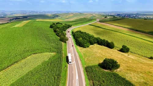 Trucking along winding road through green farmland landscape.