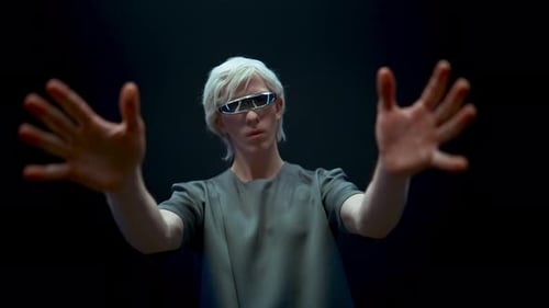 Young Man Wearing Futuristic Glasses Gesturing on Dark Backdrop