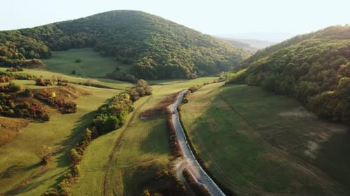 Aerial View of Winding Road Through Lush Green Mountain Valley at Sunset