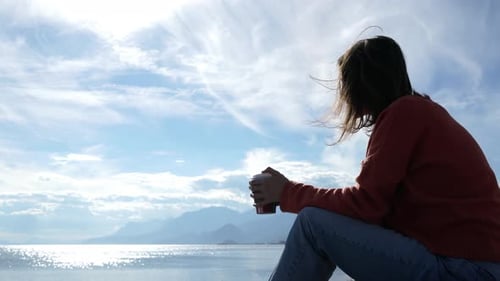 cinematic video of a person drinking coffee whilst looking out over the sea and enjoying her headspa