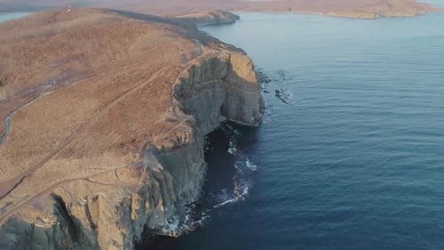 Aerial Drone View of an Ocean Blue Waves Break on High Cliff of a Rocky Mountain During the Sunset