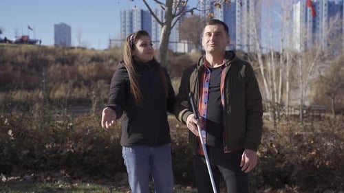 Seine Frau erzählt dem sehbehinderten Mann etwas im Park.