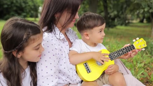 Mother and Children Play Ukulele in the Park