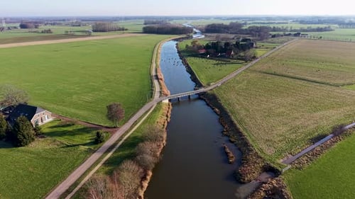 Aerial view of a rural landscape with a canal curving through green fields, two small road bridges