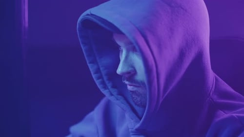 hacker in a hood works at a computer close up