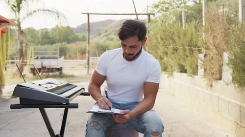 Man Writes Notes Near Keyboard in Rural Setting