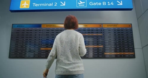 Airport Terminal Back View of Woman with Luggage Checking Flight on Digital Departure Board