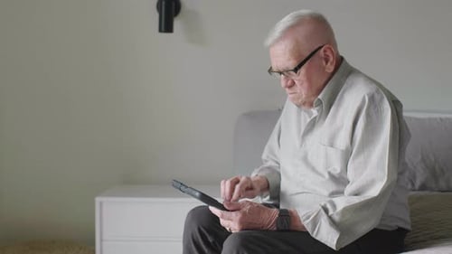 Senior Man Using Tablet Device While Sitting on Bed