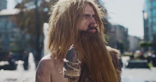 Ernster Neandertaler mit langem Bart blickt mit prähistorischer Waffe in die Kamera und jagt Tiere in