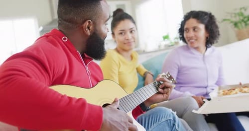 Happy, diverse female and male friends playing guitar and listening at home in slow motion