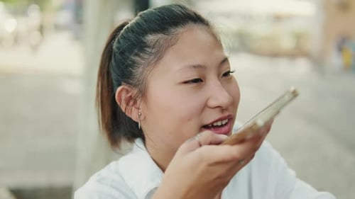 Close up, young woman sitting on bench and sending voice message using mobile phone