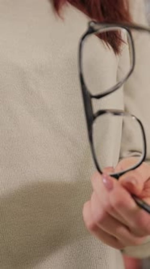 Vertical Video Individual is Elegantly Holding a Pair of Eyeglasses Emphasizing Stylish Eyewear