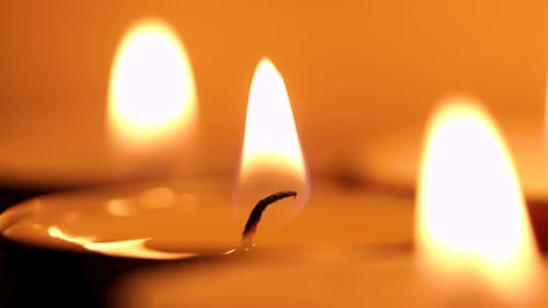 Three small candles burning slowly, beautiful flames shot in dark, romantic atmosphere. Detail shot,
