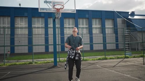 Sport Man Throws Up Volleyball Jumps and Hits It on Basketball Court with Blue Building Background