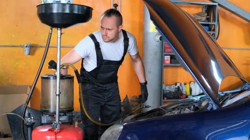 Man in Shorts and Orange Vest Works on Car with Hood Up in Garage