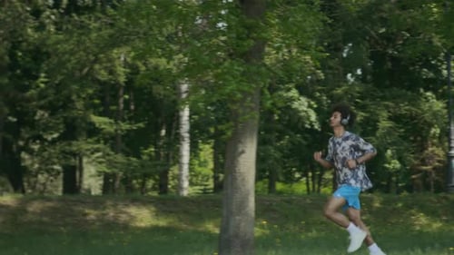 Young Man in Headphones Jogging through Park