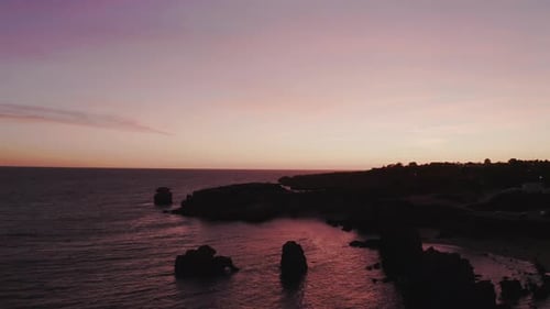 Majestic aerial backwards shot of outstanding rocks from the ocean and coastline after sunset. Golde