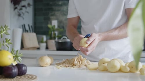 Mittlere Aufnahme eines Mannes, der in einer modernen Küche frische Kartoffeln mit einem Schäler schält