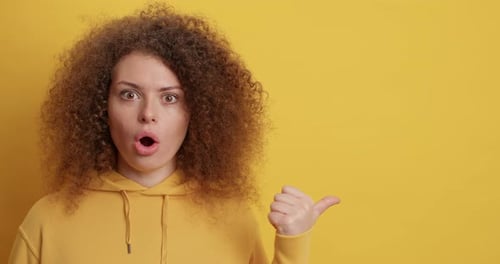 Surprised woman points to the side on yellow background