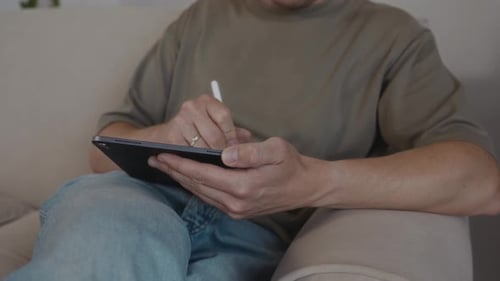 Man Using Tablet with Stylus on Sofa Indoors
