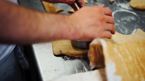 Close up over the shoulder shot of baker cutting perfectly round cookies out of rolled-out cookie do