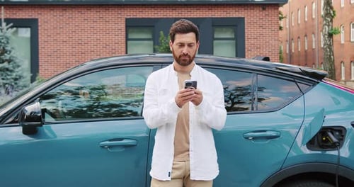 Erwachsener Geschäftsmann im Freizeitanzug lächelt und schaut in die Kamera, während er das Smartphone neben seinem El benutzt