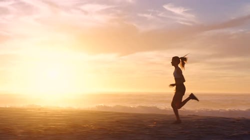 Fit, active and sporty female running, jogging and exercising on the beach during sunset in summer