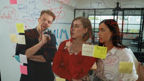 Coworkers Brainstorming Ideas Writing on Glass Whiteboard at Workplace