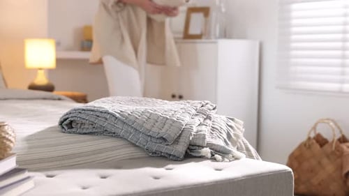 Woman putting blanket onto bed in room, selective focus. Home textile