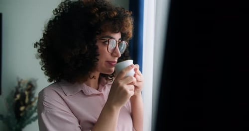 Attractive Peaceful Dreamy Woman with Curly Hair Wearing Glasses Holding Cup Enjoy Favorite Tea
