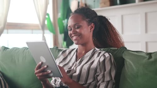 Woman Smiling Using Tablet Device on Green Couch