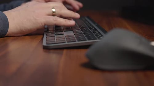 Person’s hands wearing a grey sweater and has a ring on the left handtyping on a black keyboard plac