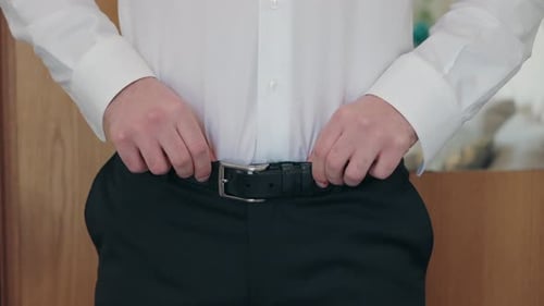 Man Adjusts His Belt in Preparation Indoors
