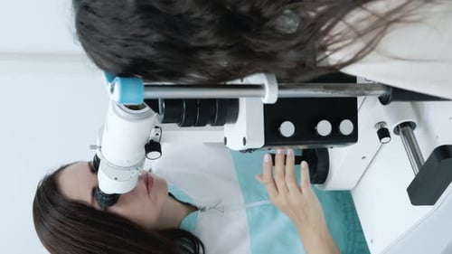 Attentive optometrist examining beautiful female patient with slit lamp in ophthalmology clinic. Opt