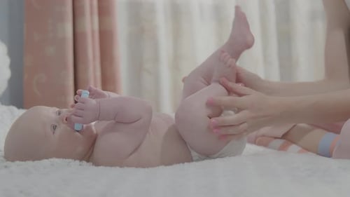 Infant Receives Leg Massage from Adult on Bed