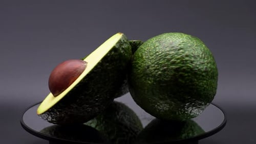 Close up shot of 3 avocados rotating on a mirror and a black background