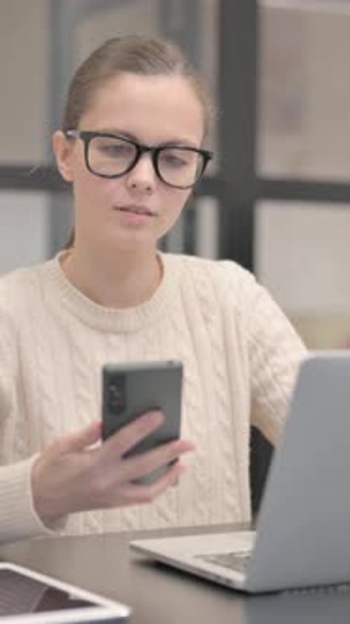 Woman using phone at desk with laptop