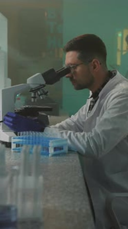 Close Up Scientist with Glasses and Protective Gloves Looking in the Microscope in the Laboratory