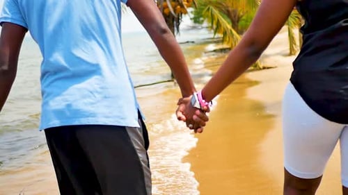 Couples walking and holding hands on a sandy beach with waves coming in