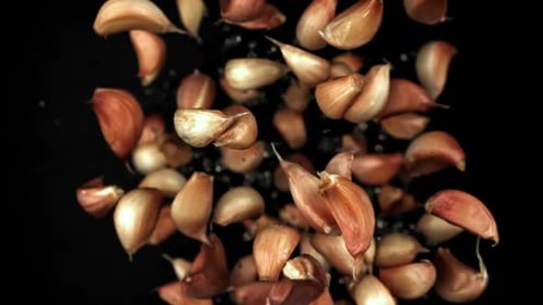 Los dientes de ajo vuelan y caen sobre un fondo negro filmados con una cámara de alta velocidad a 1000 fps